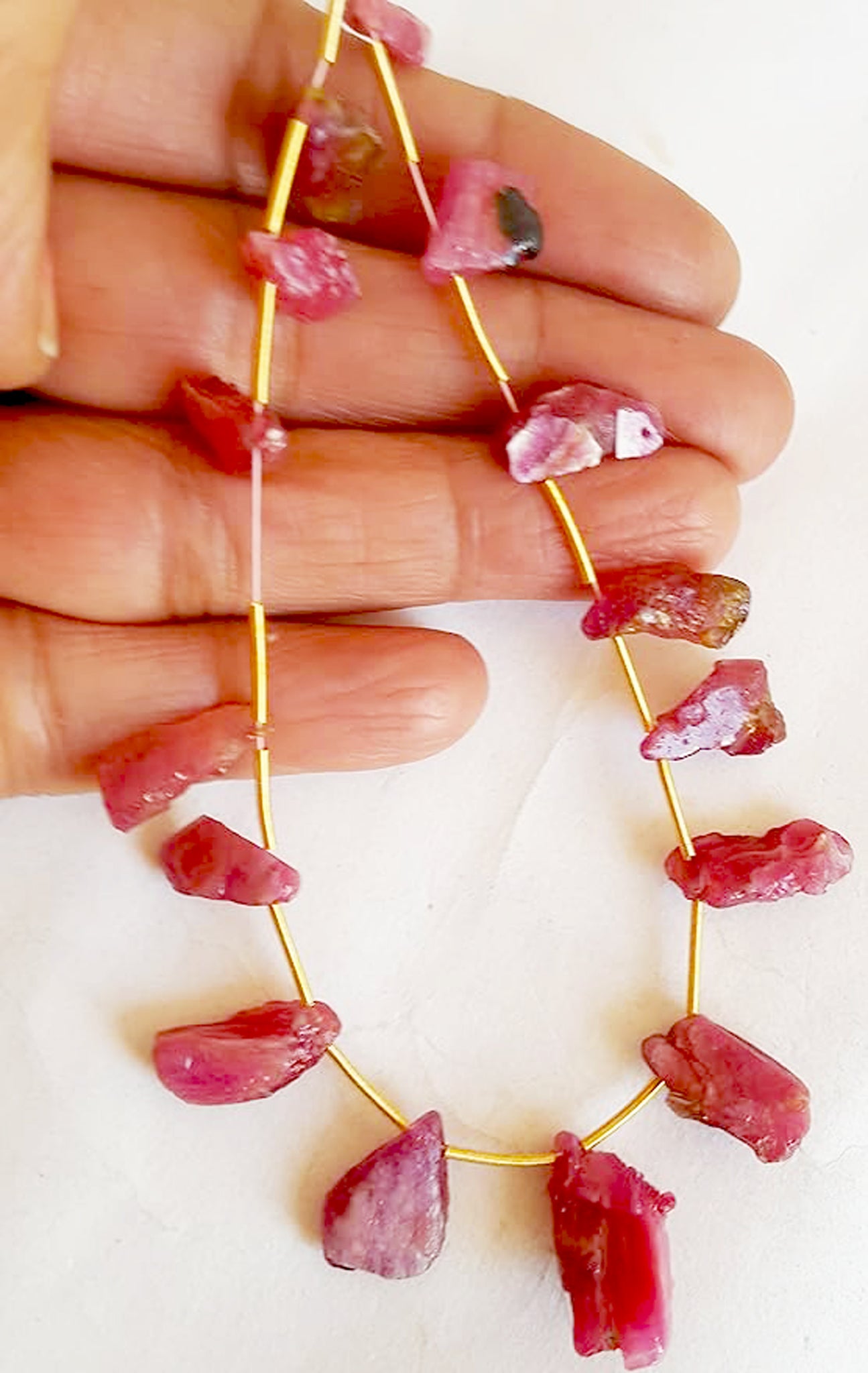 A person holds delicate strands of ruby beads, showcasing their smooth design.