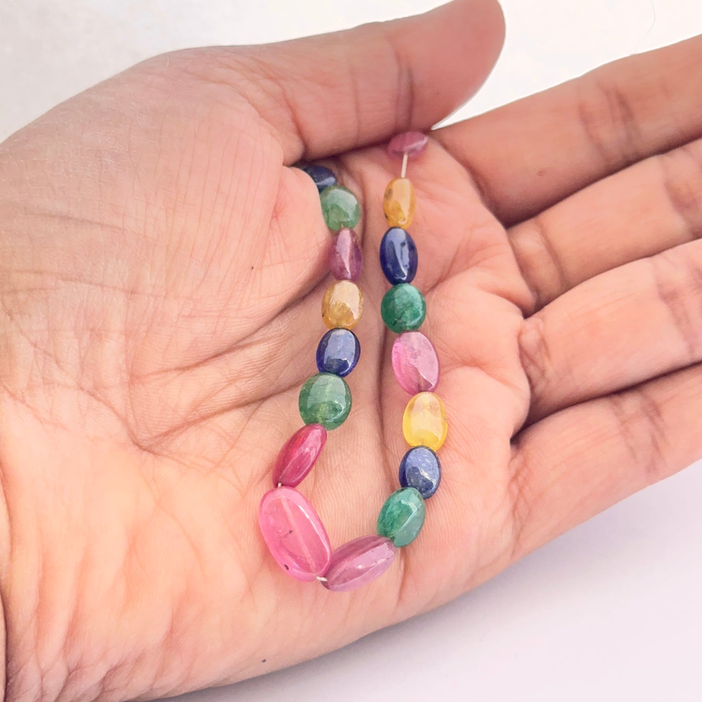 A person holds the multi precious smooth oval bead set, showcasing yellow sapphire, blue sapphire, ruby and emerald.