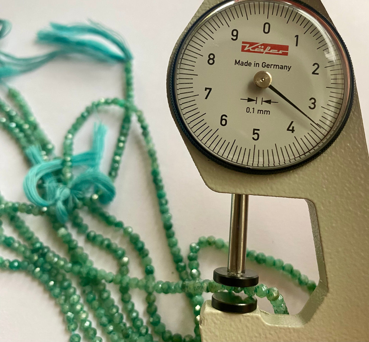 Close-up of a measuring dial gauge alongside green amazonite beads, showcasing their faceted rondelle shape and size.