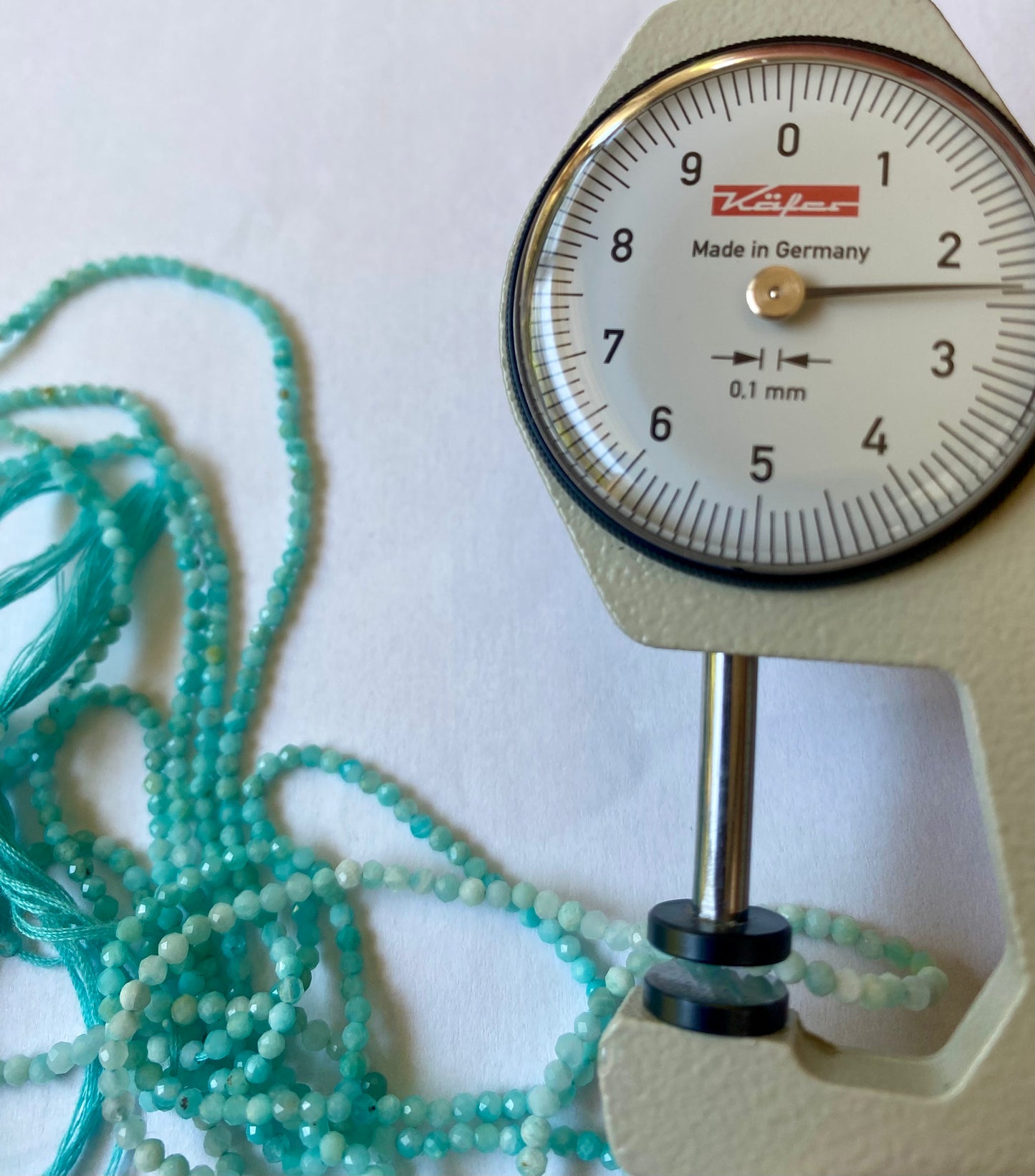 A dial gauge displaying a blue bead beside a gemstone strand made of faceted rondelle spinel beads, 2.2mm to 2.5mm in size.