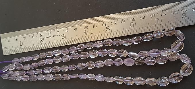 A person measures a purple amethyst stone, ranging from 8mm to 9mm, using a measuring tool, ruler.