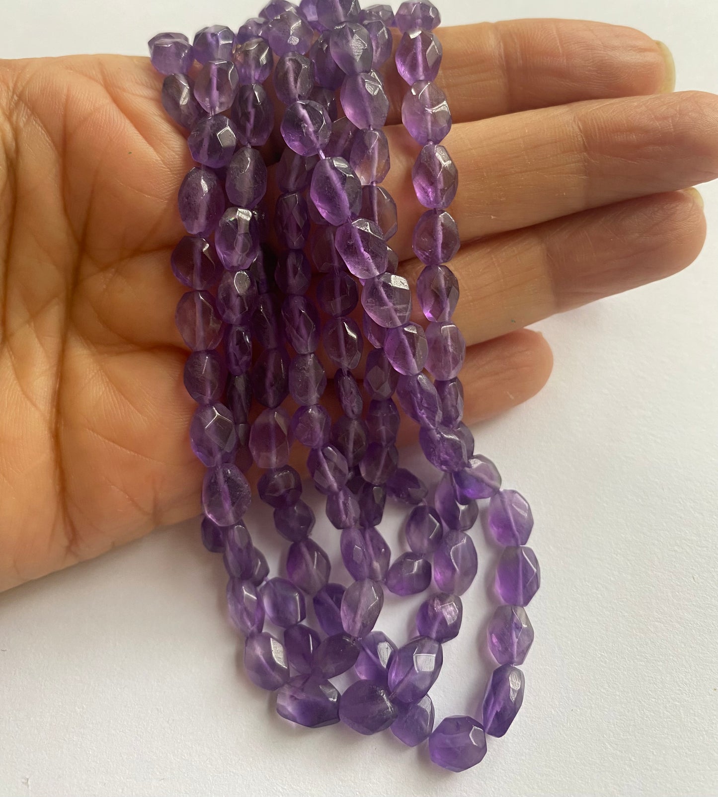 A person holding a amethyst gemstone strand, showcasing its purple facets and elegant design.