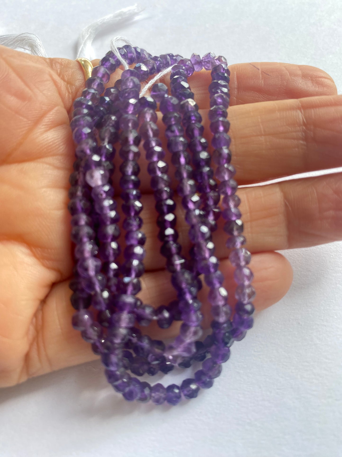 A person holding a faceted rondelle amethyst gemstone strand, showcasing its purple facets and elegant design.