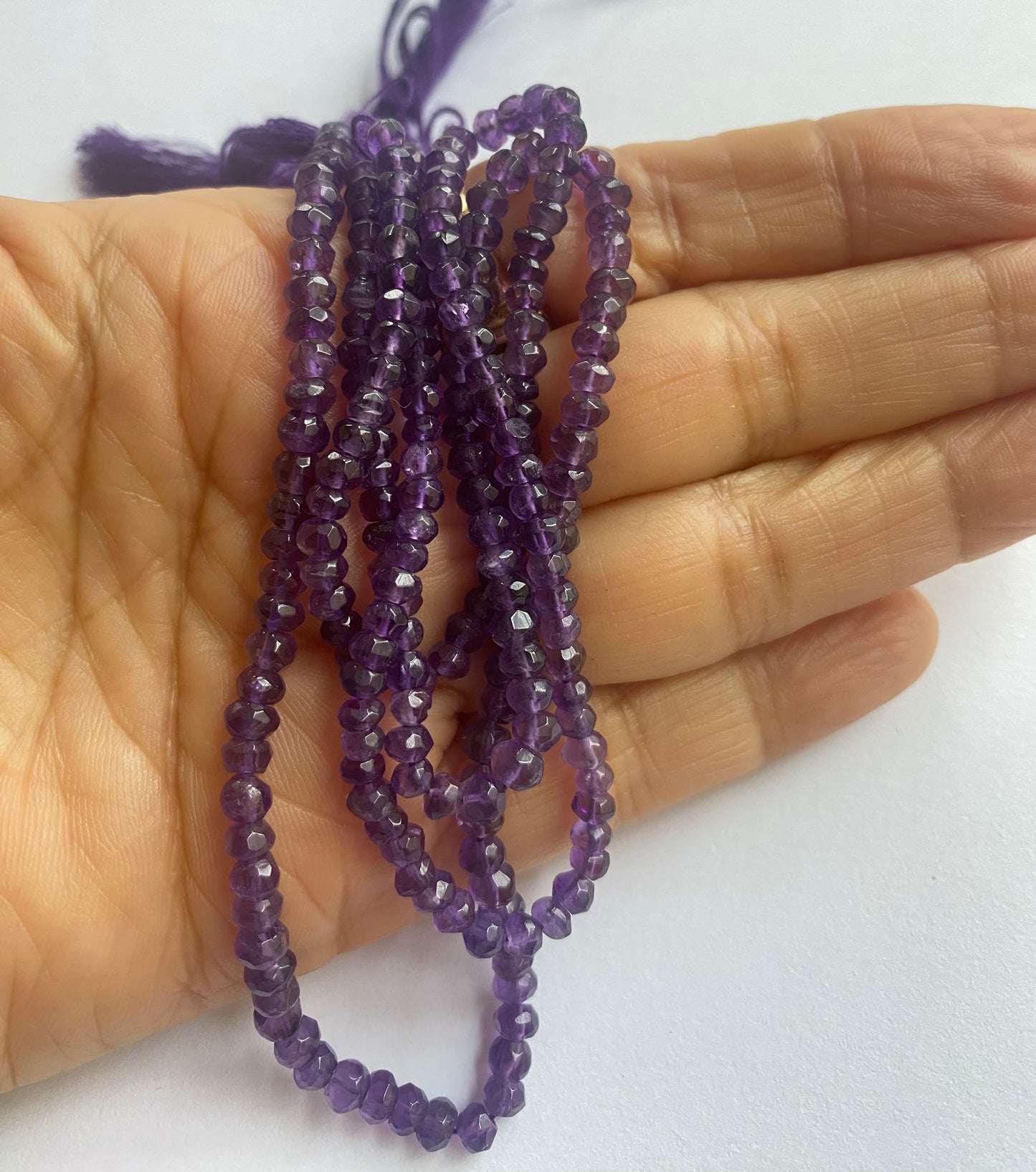 Close-up of a person holding a stunning purple faceted rondelle amethyst gemstone strand, highlighting its intricate facets.