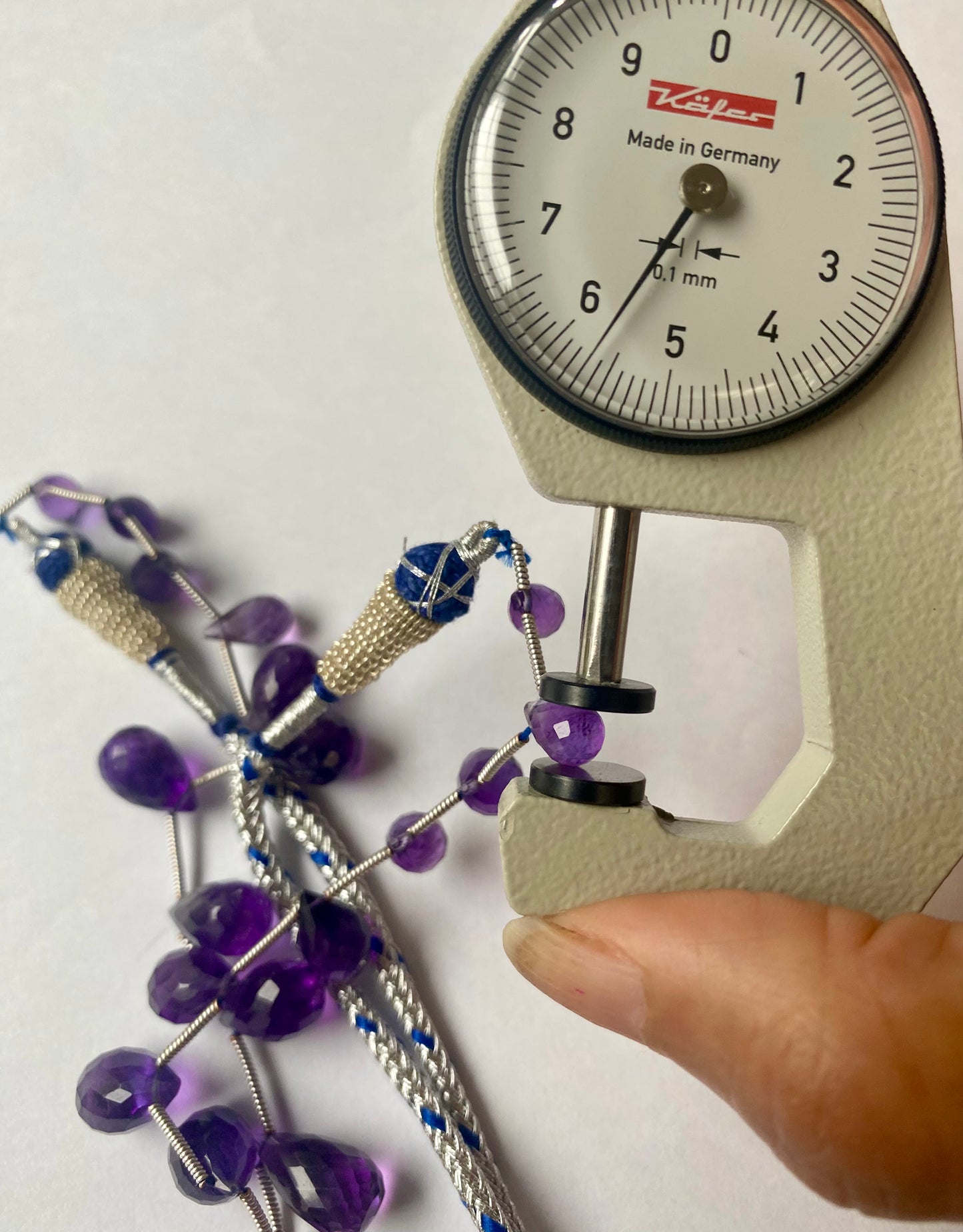 A close-up of a person measuring a purple amethyst teardrop stone, 5mm to 8mm, with dial gauge.