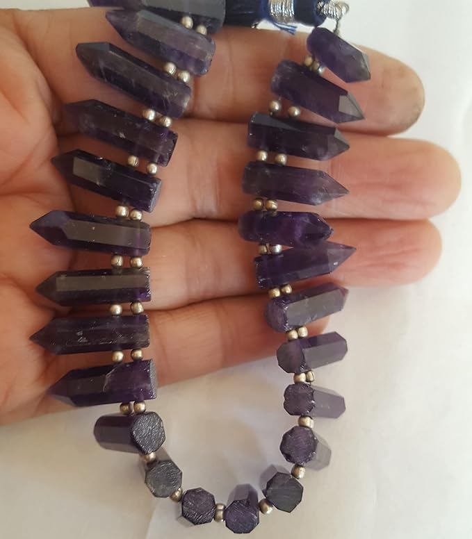 A hand holds a stunning purple strand made of smooth pencil gemstones.