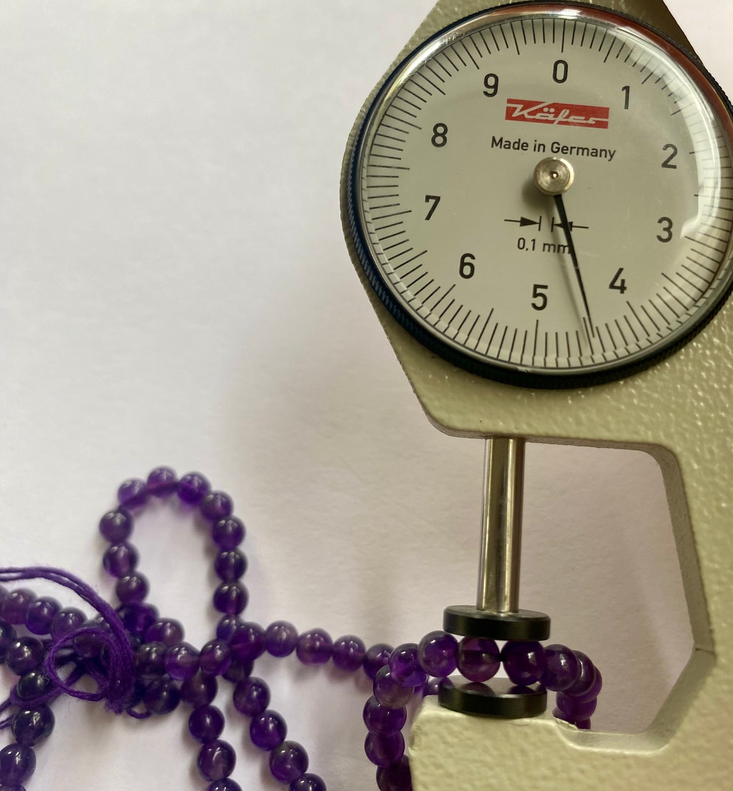 A person measures a purple amethyst smooth round stone, using a dial gauge measuring tool.