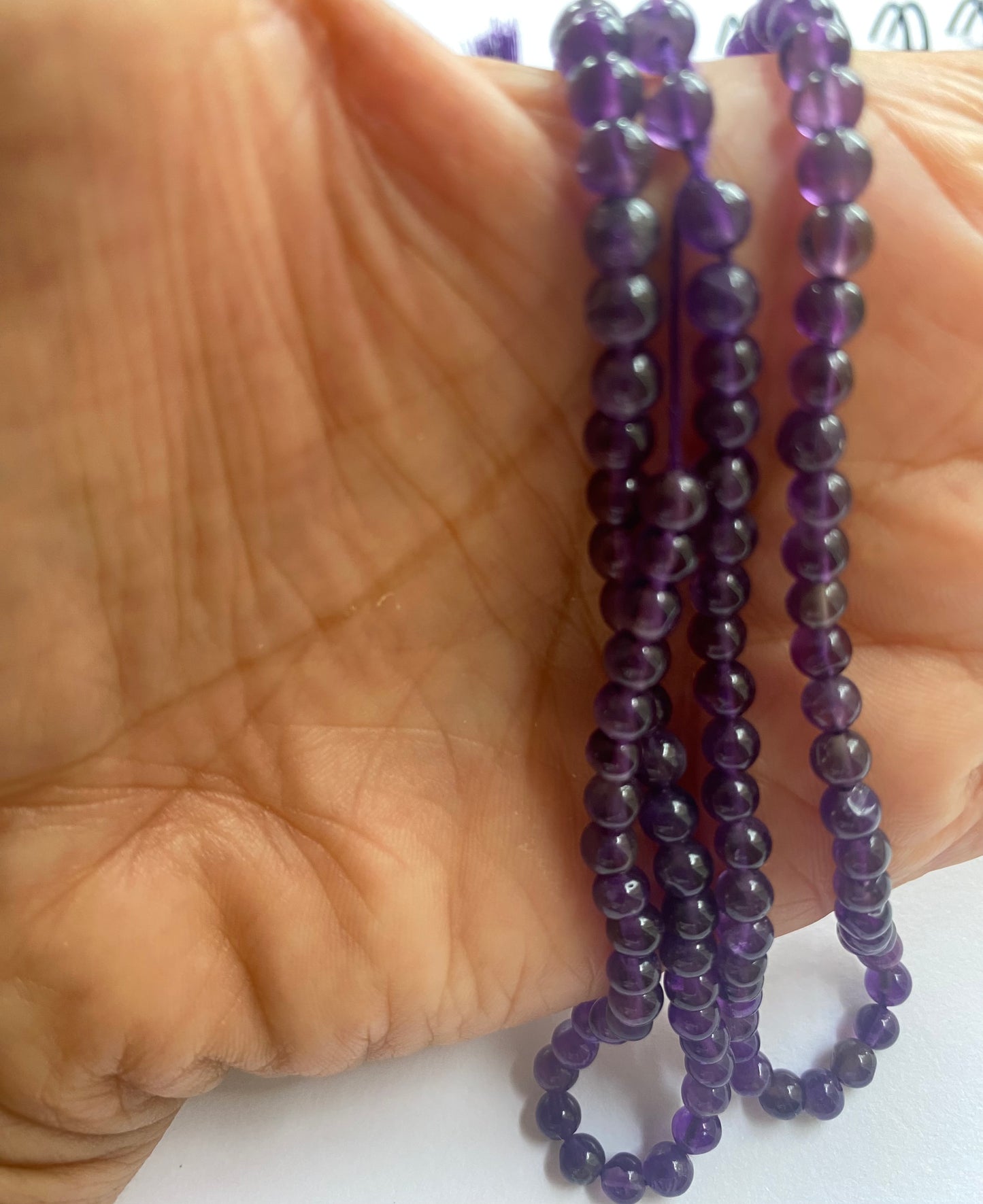 A person holding a smooth round amethyst gemstone strand, showcasing its purple facets and elegant design.