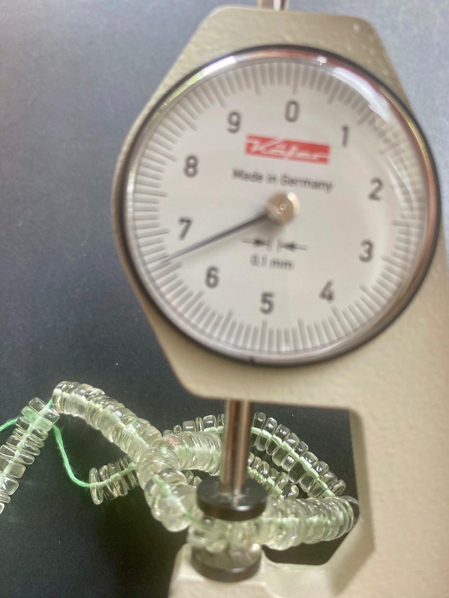 A person measures amethyst Smooth wheel stone, ranging from 56.5mm-7.0mm, using a dial gauge measuring tool.
