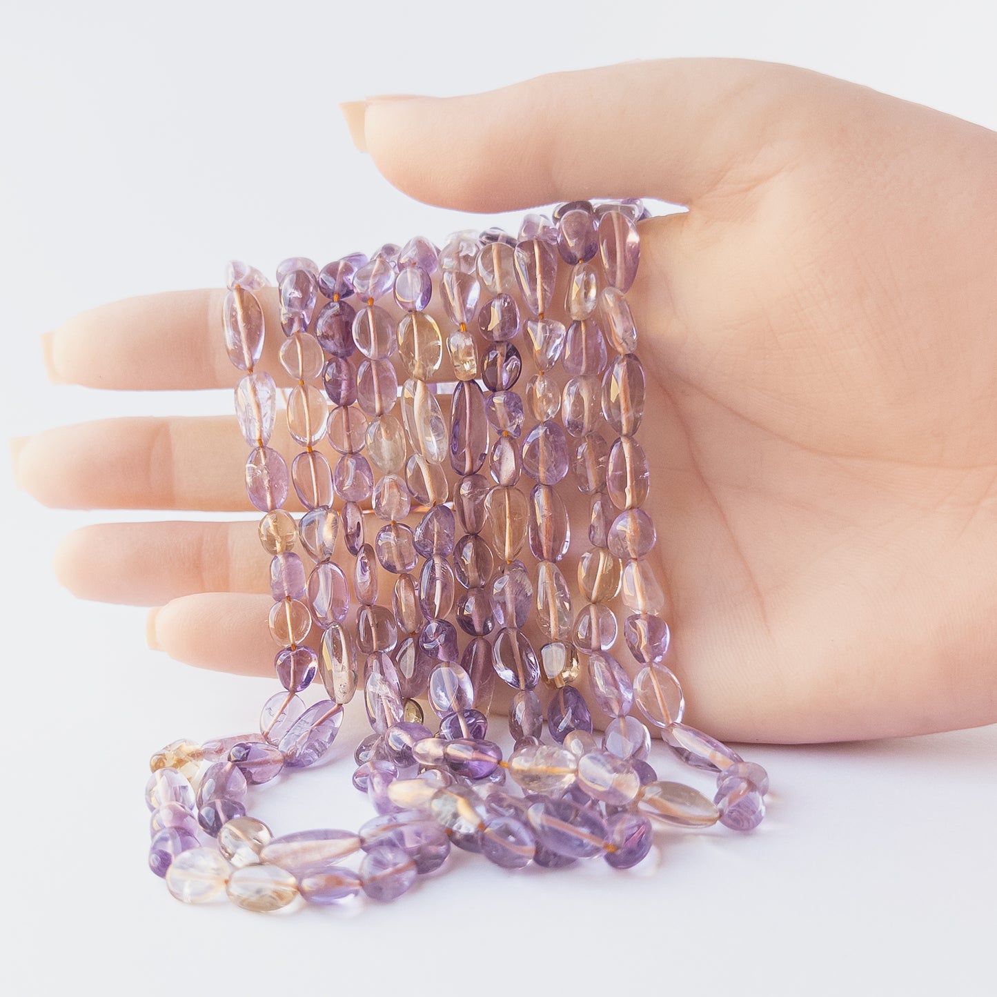 A person holds delicate strands of Ametine beads, showcasing their smooth tumble design.