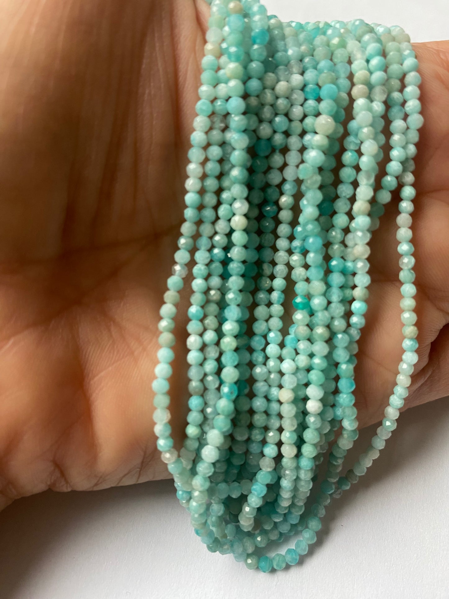 A person holding a strand of Aquamarine faceted rondelle beads, showcasing their natural beauty and shine.