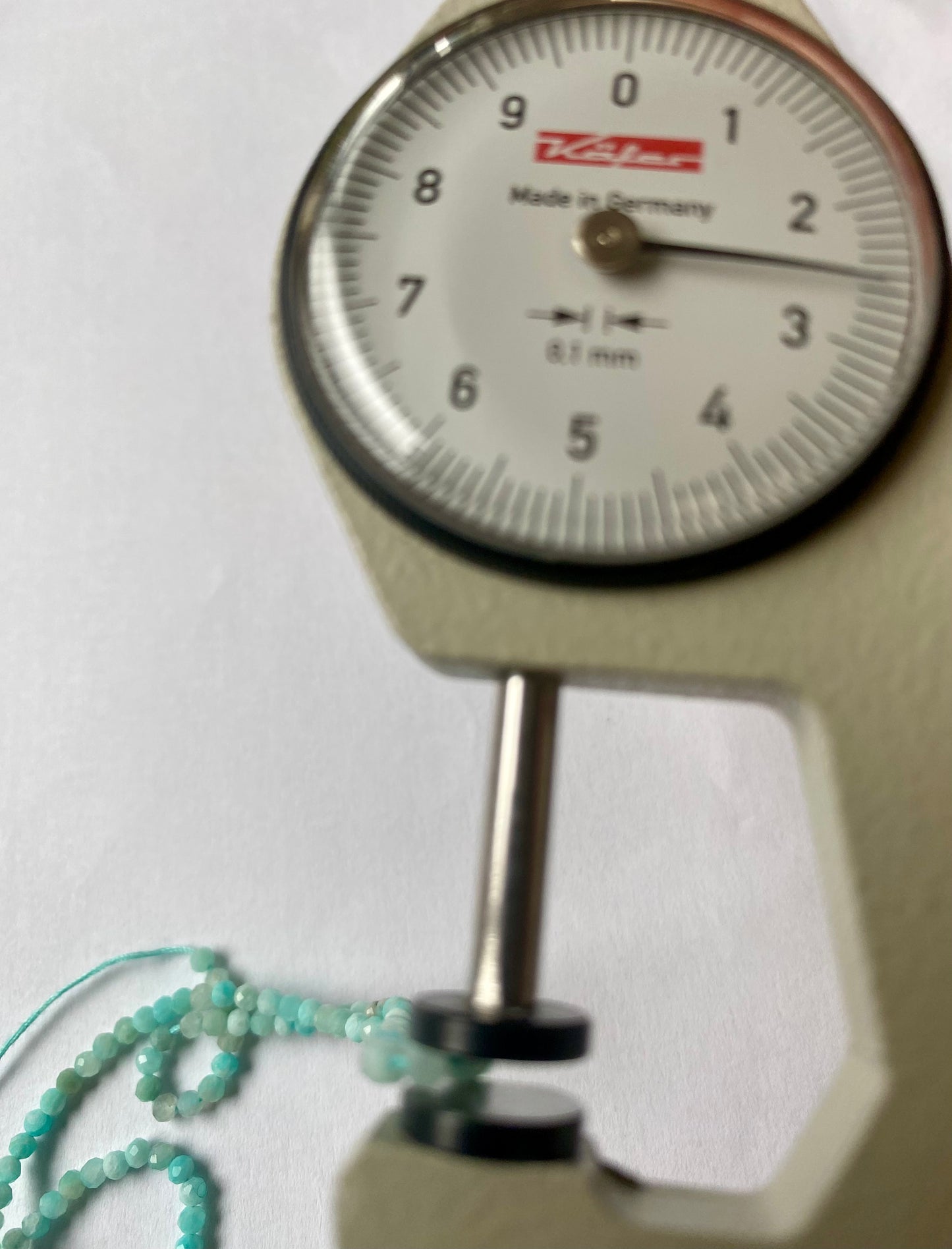 Detailed shot of a dial gauge e and faceted Aquarmarine beads, sized 2.5mm to 2.7mm, showcasing their size.