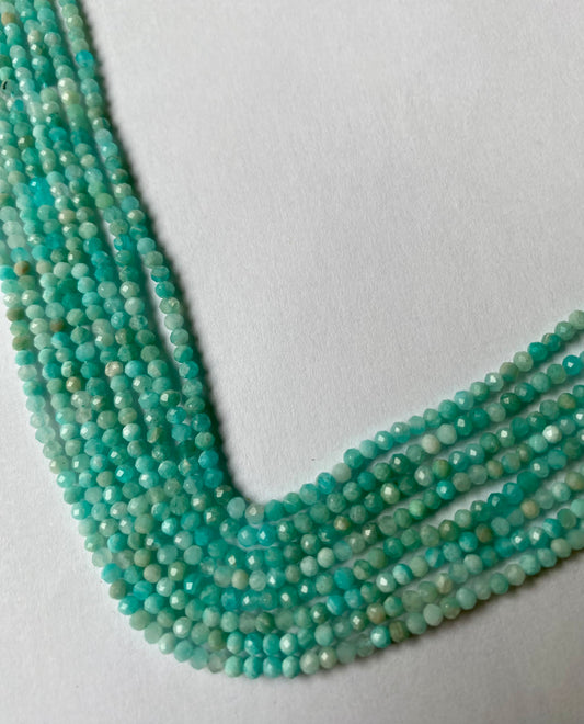Gemstone beads in cool aquamarine shades with sparkling facets, 2.7mm rondelle cut on white surface.
