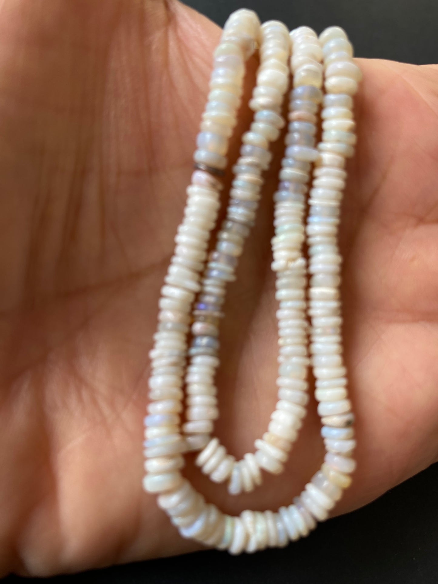 Close-up of a person grasping a strand of smooth white Australian Opal beads, each 4-4.5mm in size, highlighting their beauty.