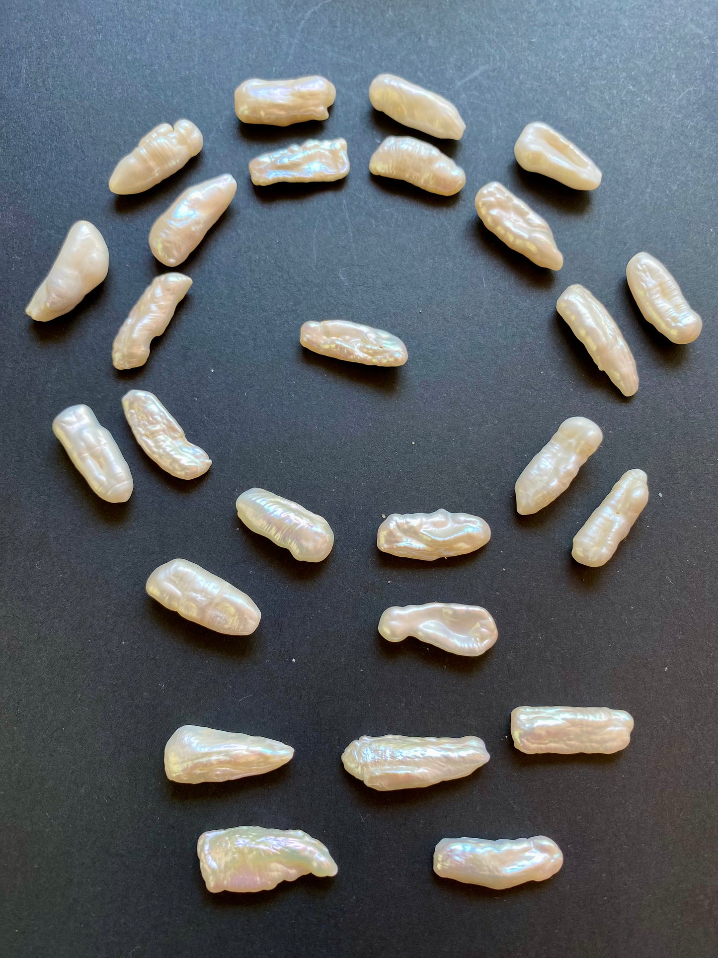 A circle of loose undrilled Baroque white pearls arranged on a smooth black surface, highlighting their unique shapes and lustre.