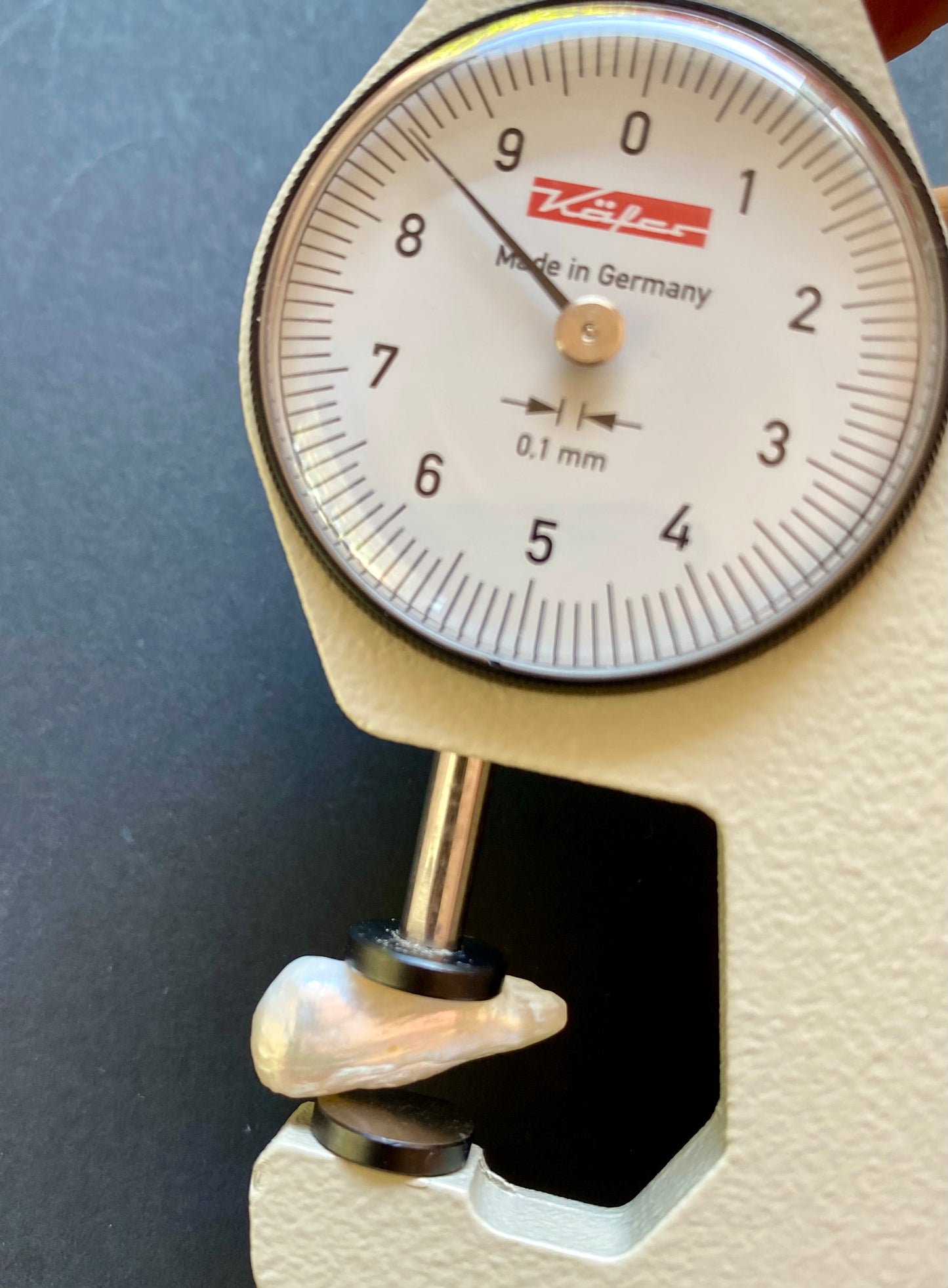 A person weighing a small white undrilled Baroque pearl on a scale, showcasing its delicate beauty and unique shape.