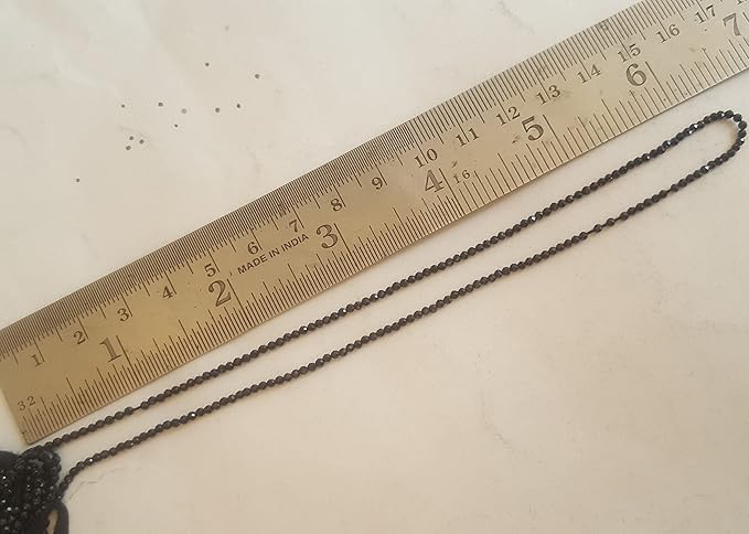 A ruler displaying a black bead beside a black gemstone strand made of faceted rondelle spinel beads, 2mm in size.