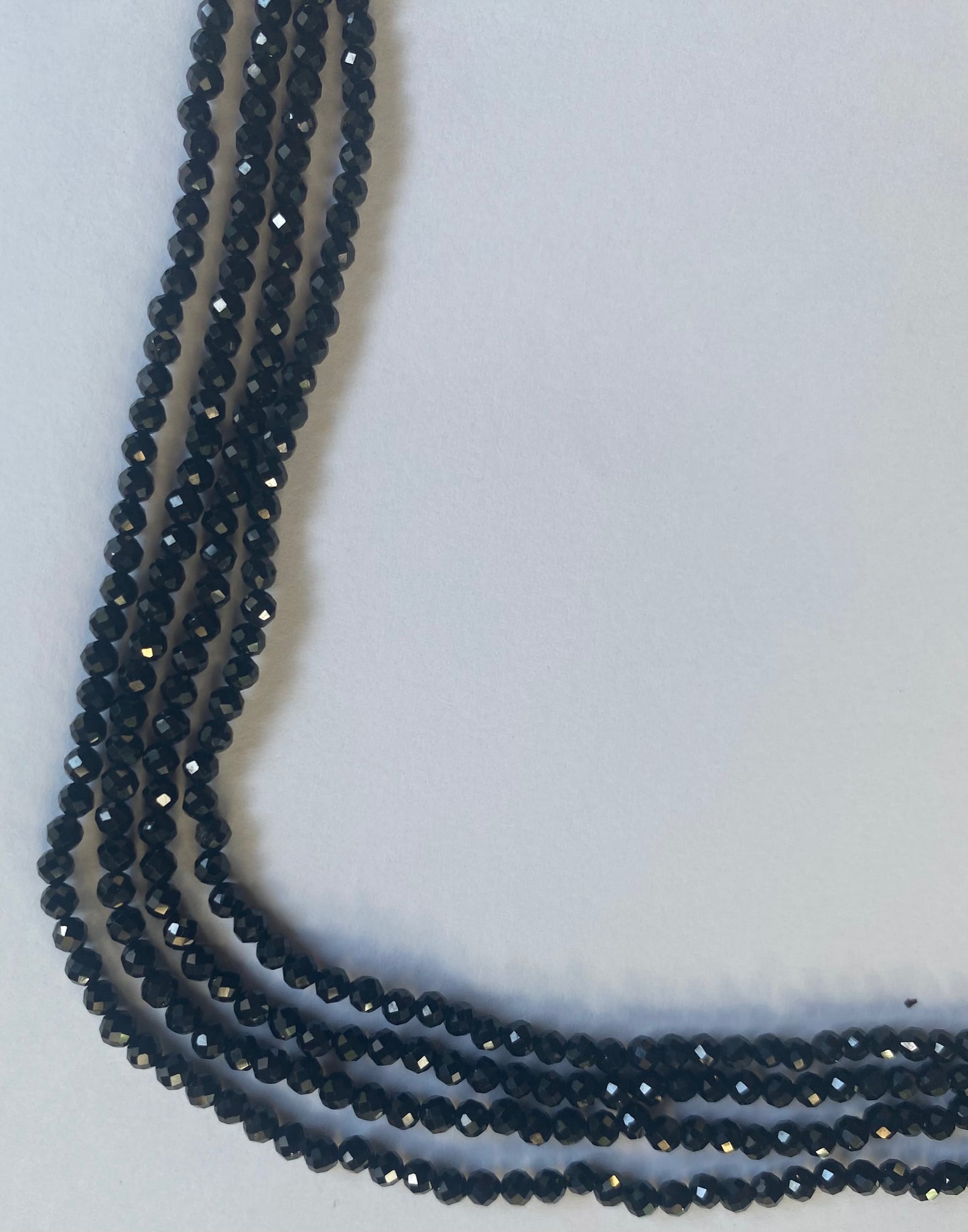 A close-up of a multiple strands featuring black spinel micro-faceted rondelle semi-precious gemstone beads.
