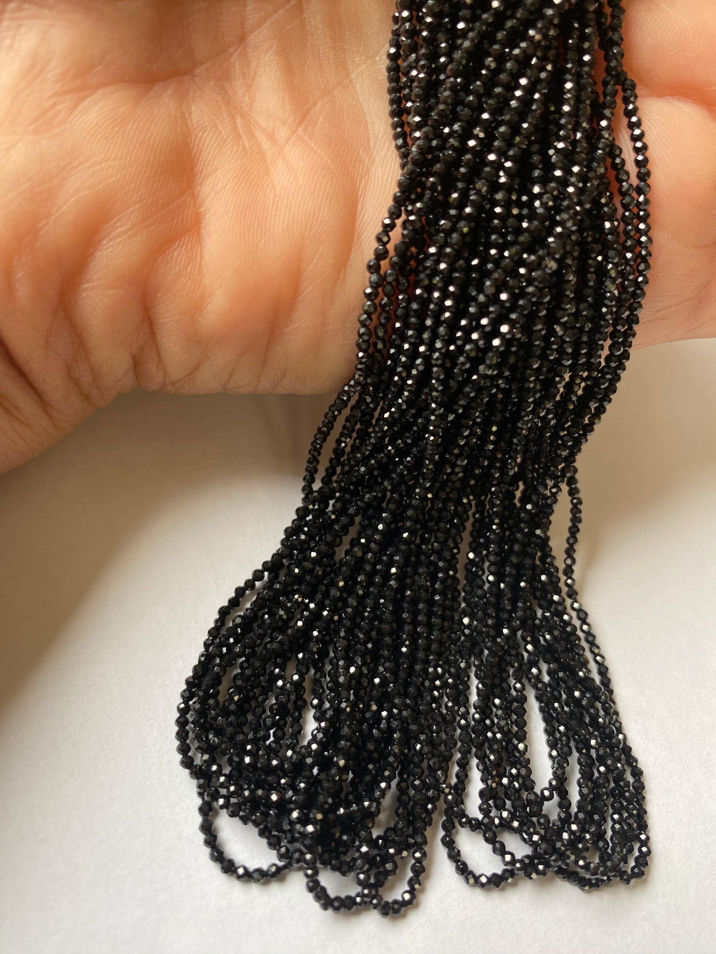 A person holding a strand of black spinel micro-faceted rondelle beads, measuring 2-2.5mm in size.