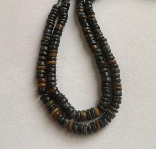 A vibrant strand adorned with black tiger eye beads, elegantly placed on a smooth white surface, emphasising its bold aesthetic.