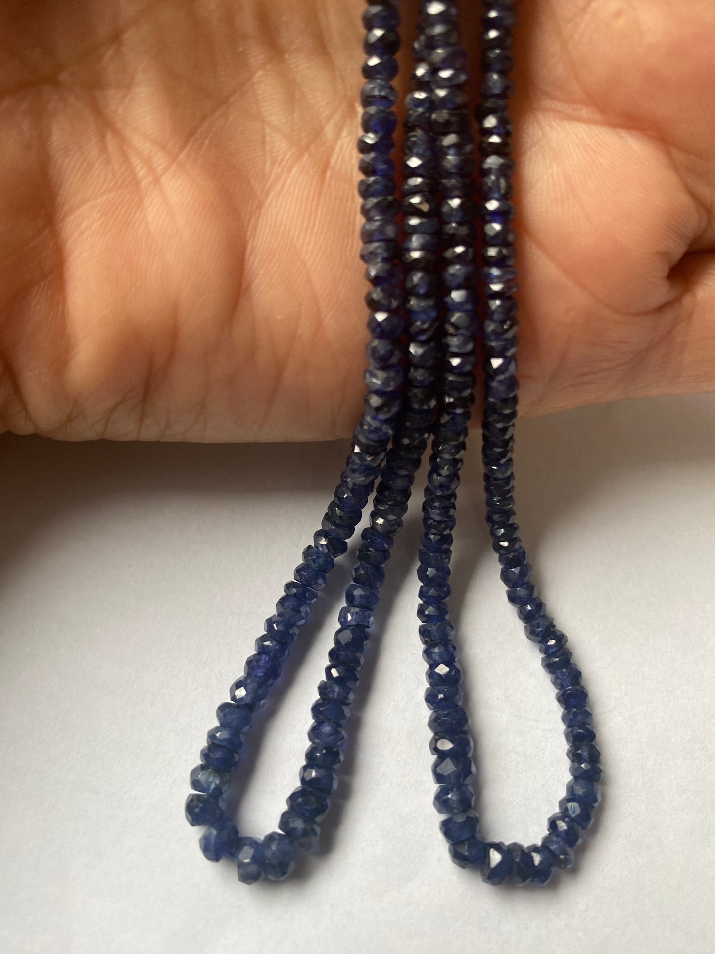 A person holding a strands of faceted blue sapphire rondelle precious gemstone beads, showcasing their vibrant colour and shine.