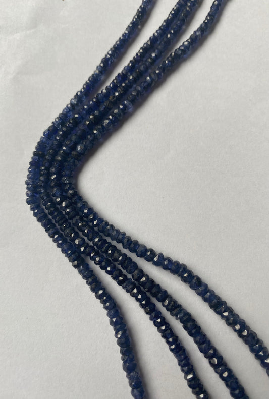 A close-up of a multiple strands of blue sapphire gemstone beads, faceted rondelles ranging from 2.5mm to 5mm, glistening in the light.