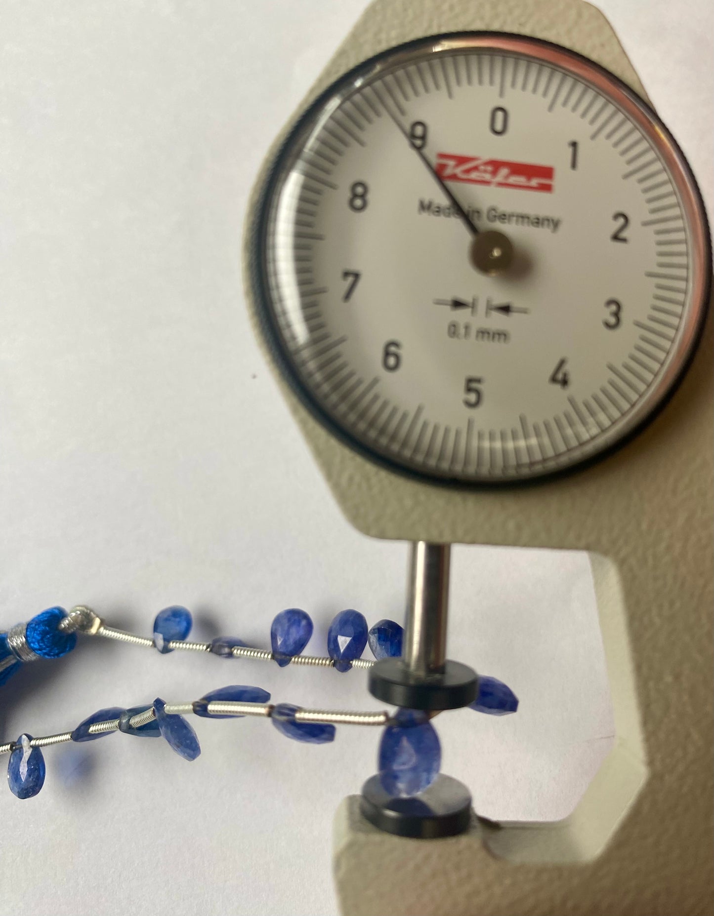 A blue sapphire faceted pear almond shaped bead with a dial gauge measure, showcasing its size and detail
