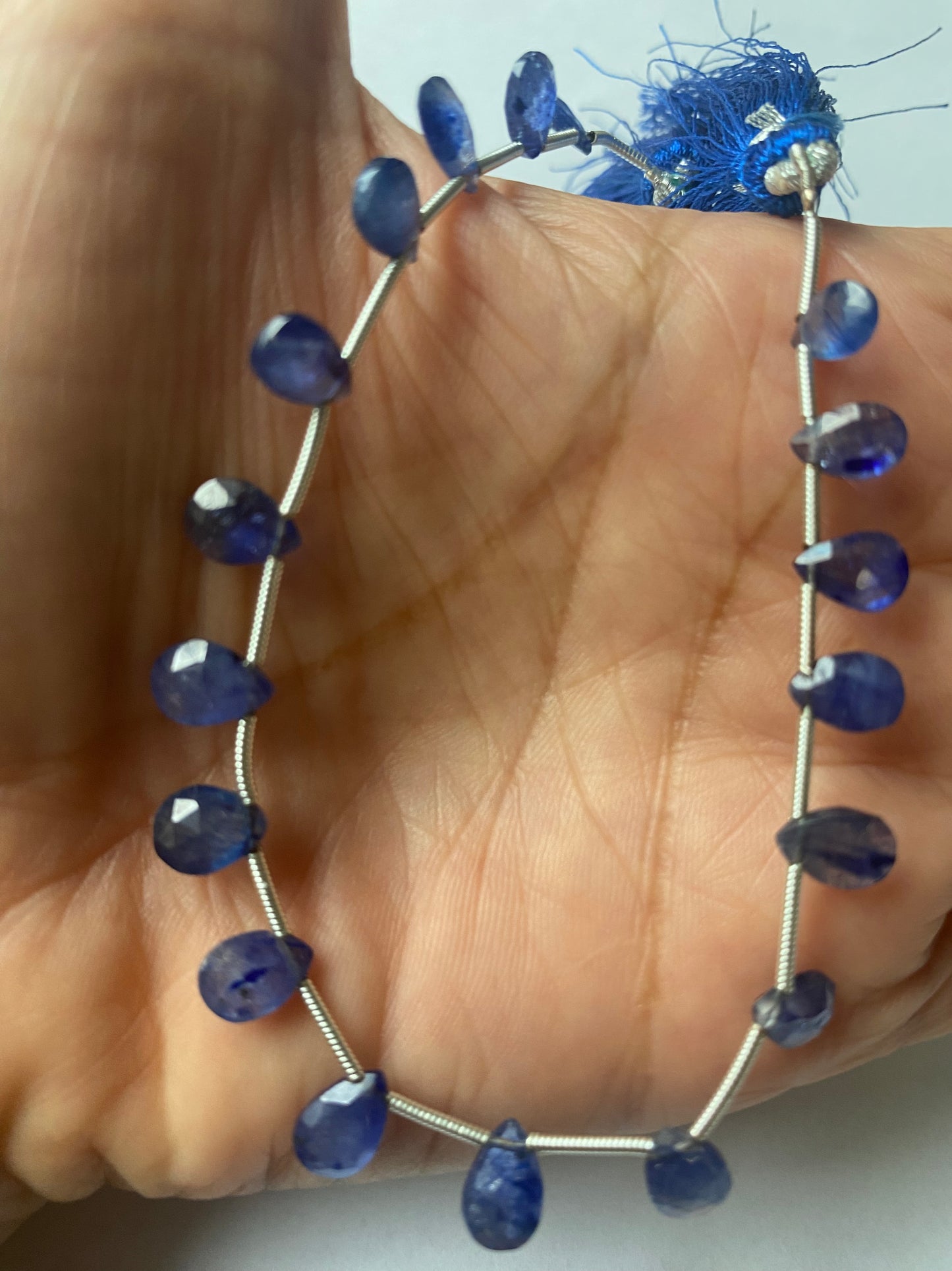 A person holding a strands of faceted blue sapphire pear shaped precious gemstone beads, showcasing their vibrant colour and shine.