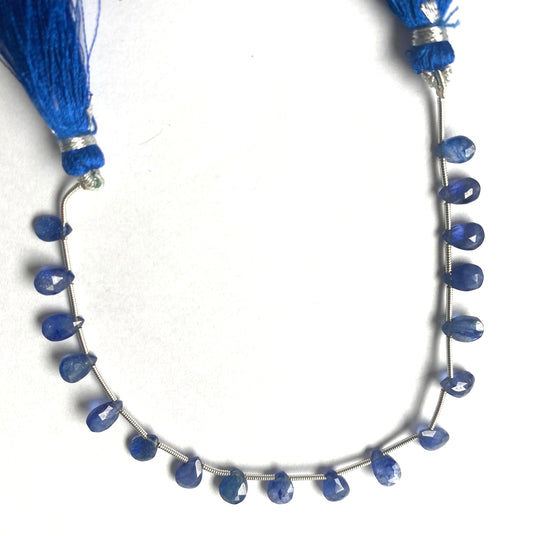 A close-up of a strand of blue sapphire gemstone beads, faceted pear shaped ranging from 7mm to 9mm, glistening in the light.