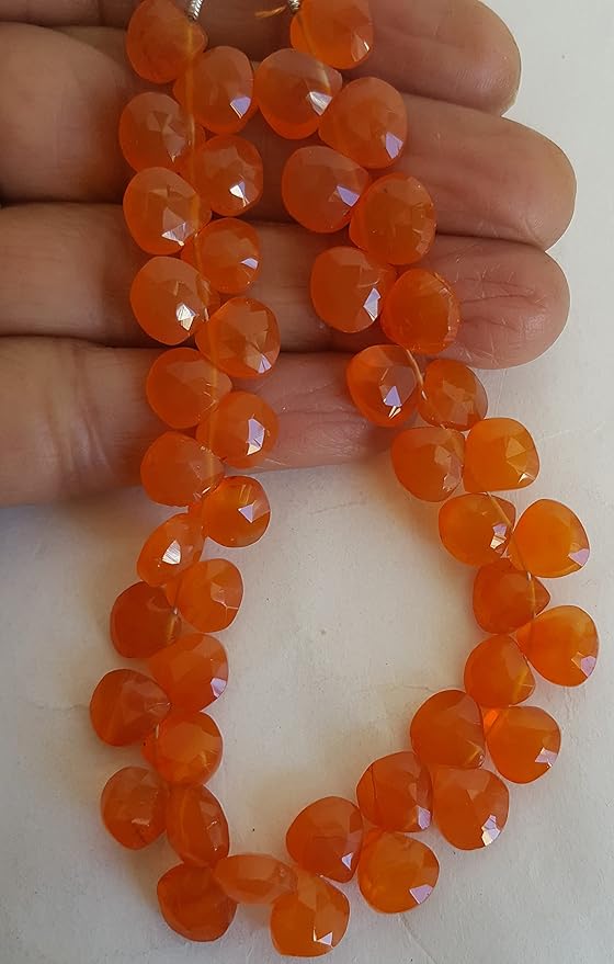 A hand holding a cluster of Carnelian gemstone beads, showcasing their briolette shape and vibrant colour.