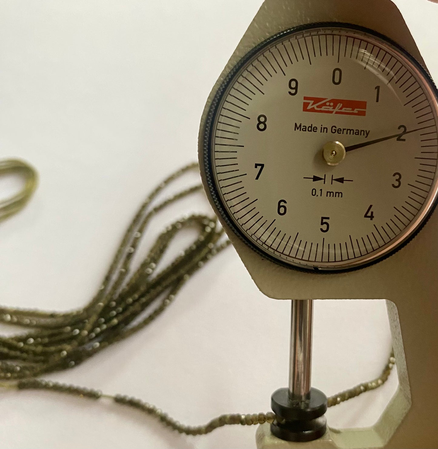 Close-up of a measuring dial gauge tool alongside a string, highlighting the precision of measurements for Cats eye jewellery.