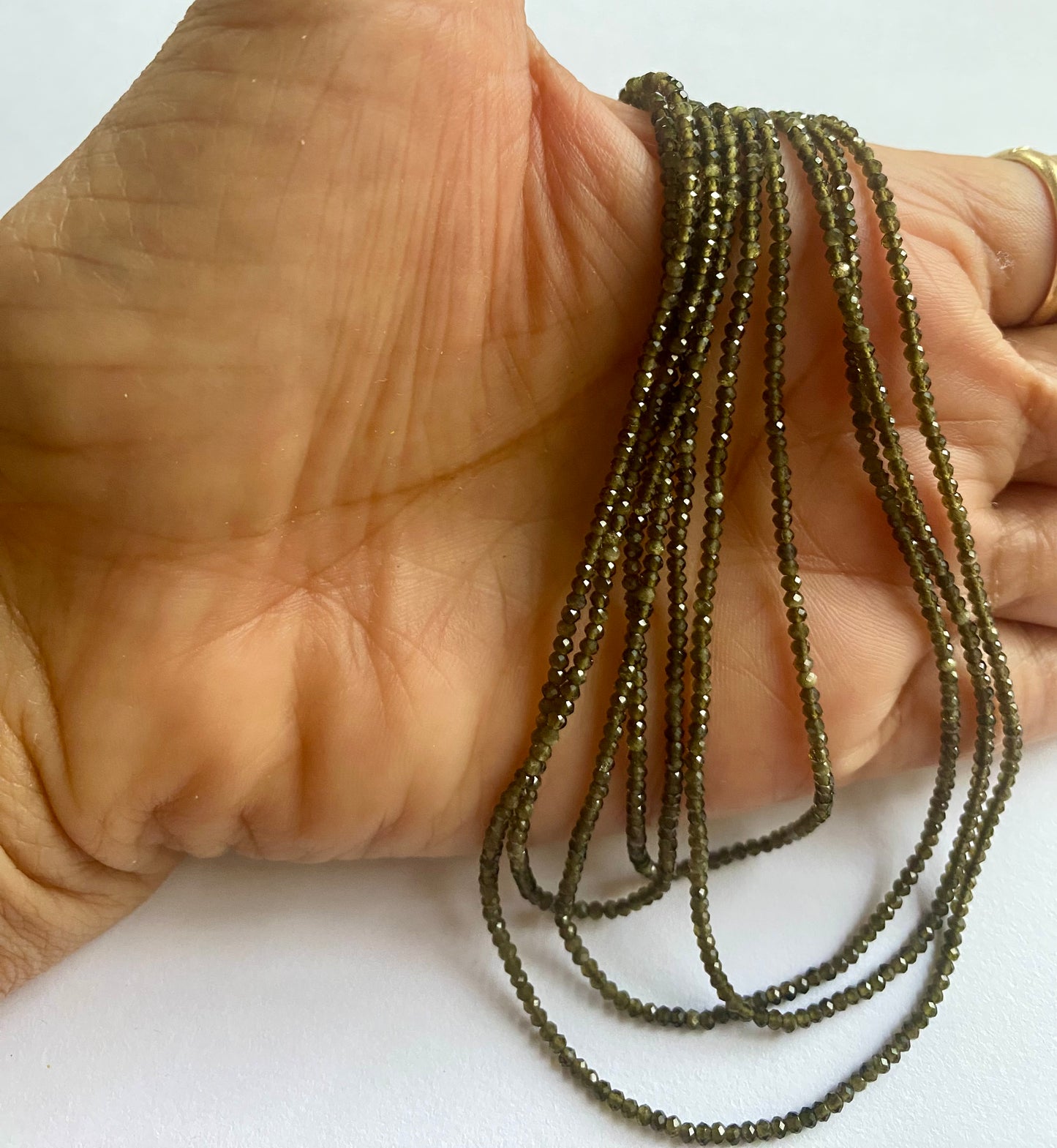 A person holding a smooth strand of Cats eye Faceted Rondelle beads, measuring 2mm, showcasing their elegant white colour.