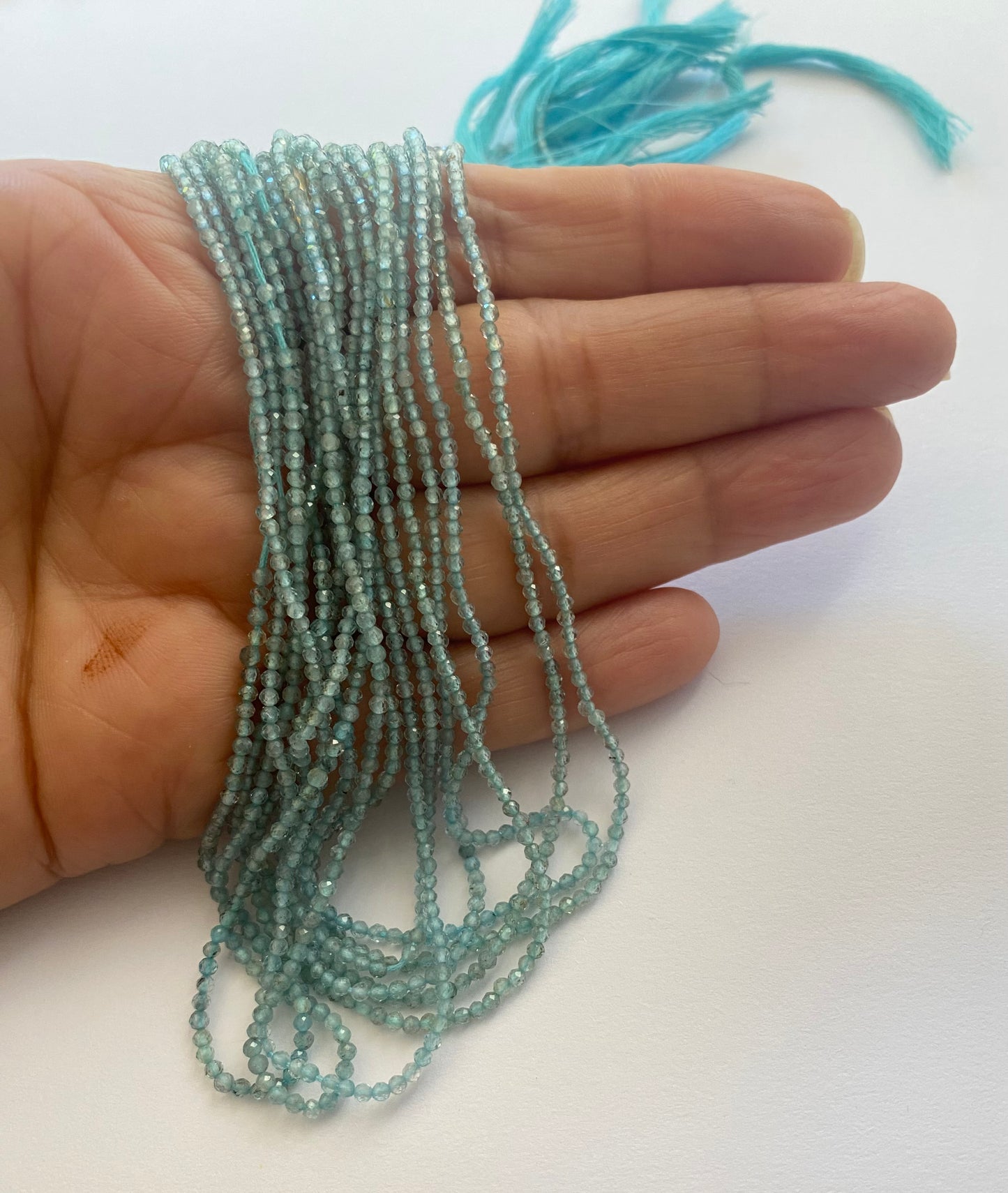 A person holding strands of chalcedony faceted rondelle beads, measuring 2mm in size.