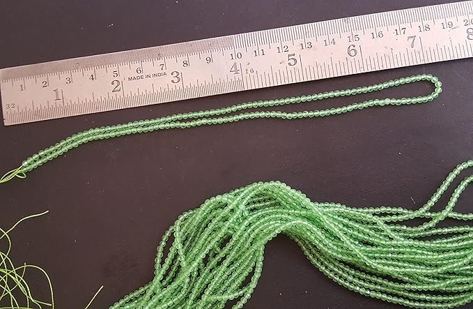 Close-up view of a measuring ruler next to green Chalcedony beads, emphasising their 2.5mm faceted rondelle shape & stand length.