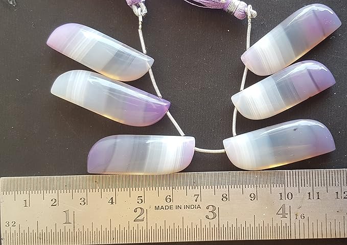 A person measures a purple Chalcedony fancy shaped stone, using a ruler measuring tool.