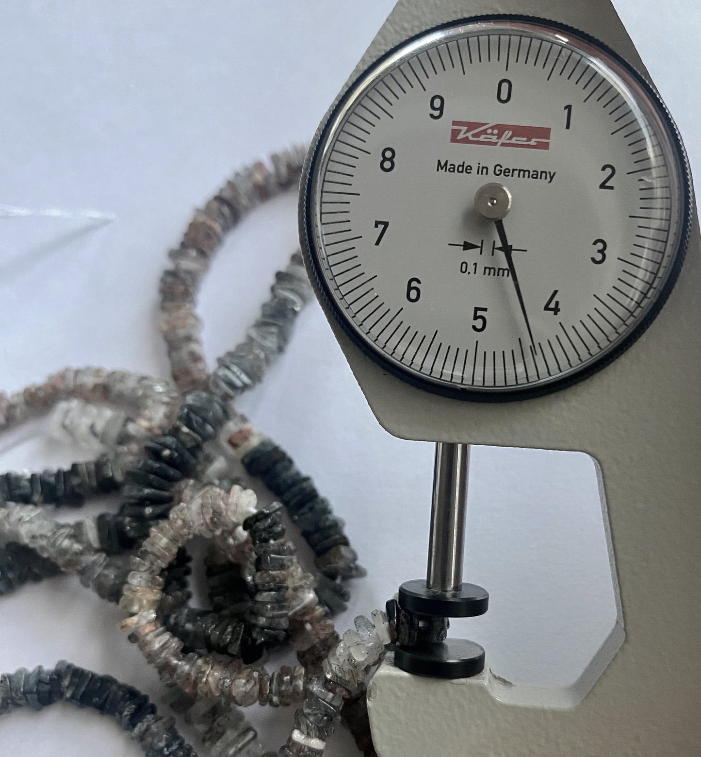A dial gauge measures the Change Garnet smooth square heishi 5–5.5mm gemstone.