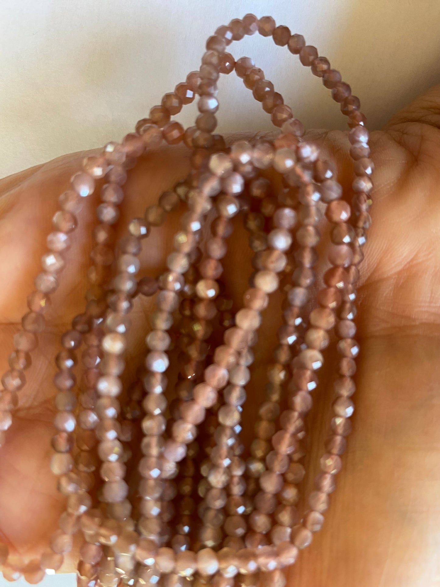 A person holding a faceted rondelle moonstone gemstone strand, showcasing its brown facets and elegant design.