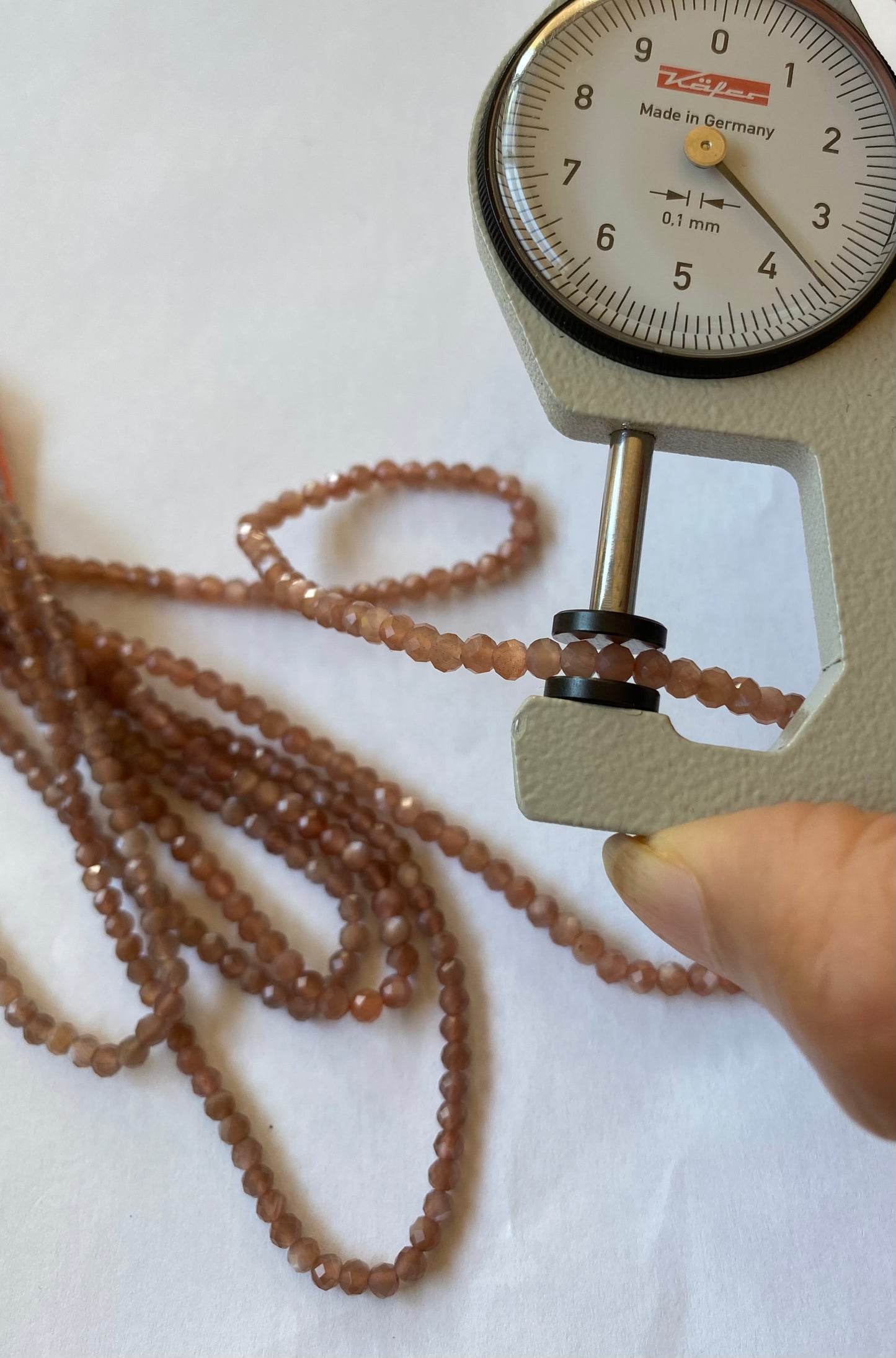 A person measures a chocolate Moonstone faceted rondelle stone, 3.5mm using a dial gauge measuring tool.