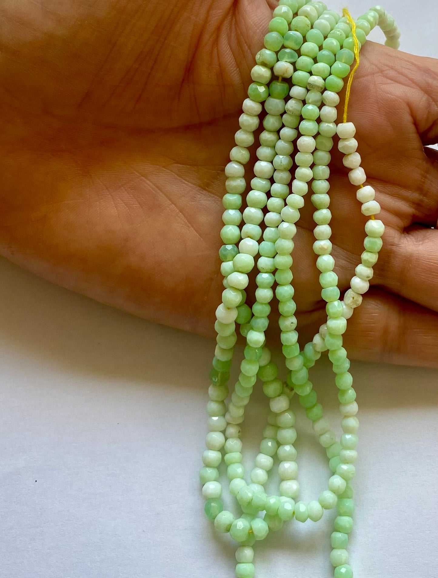 A hand displays a assortment of faceted beads, featuring green Chrysoprase gemstone.