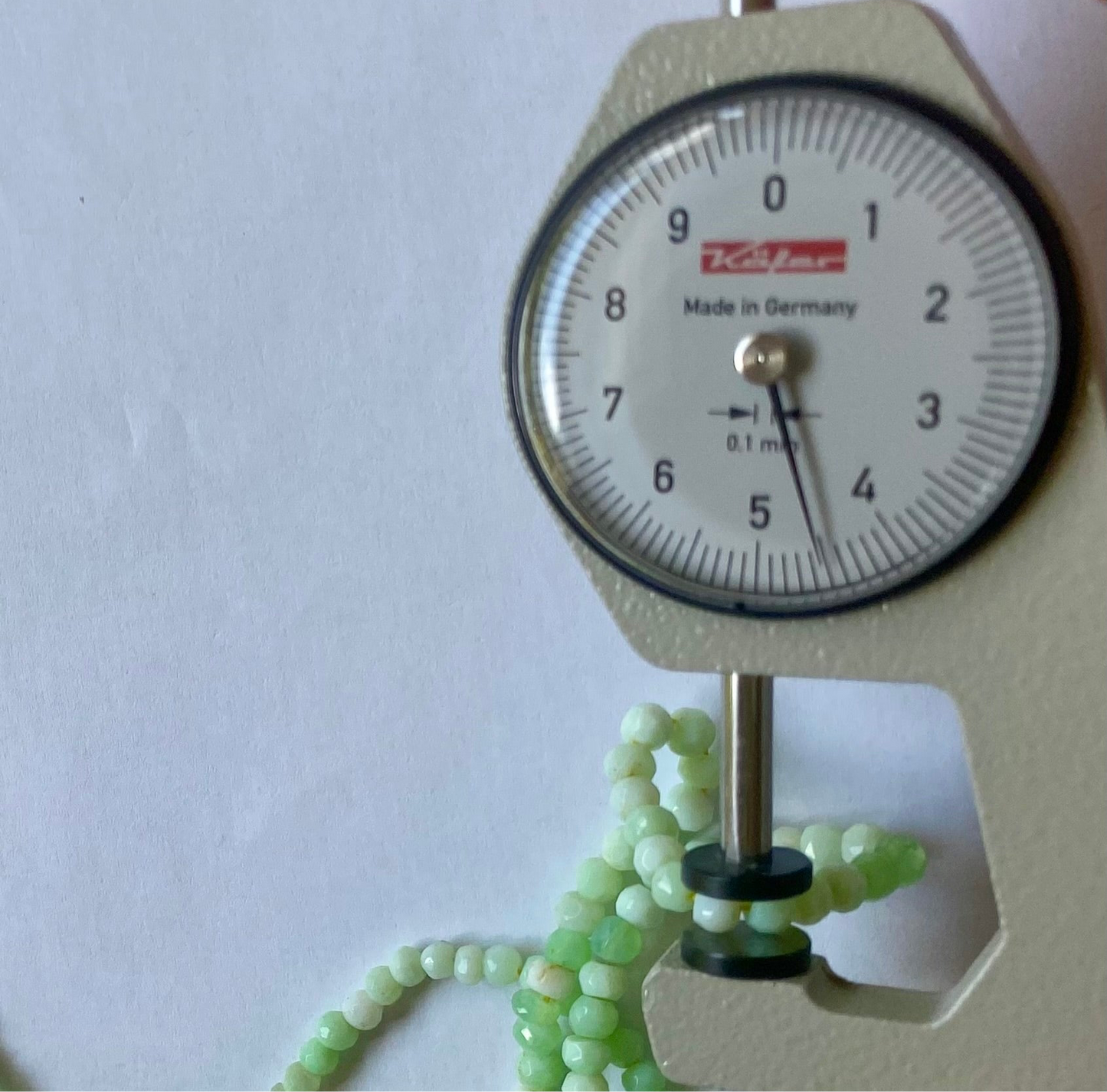 A dial gauge with a green bead on it next to Chrysoprase gemstone strand featuring 4-4.5mm faceted rondelle beads.