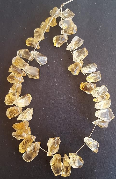 Citrine gemstone bead strand with irregular golden-yellow translucent stones, arranged in a loop on a black background. Natural inclusions add a rustic, hand crafted aesthetic.