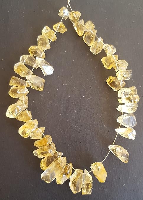 Close up Citrine gemstone bead strand with irregular golden-yellow translucent stones, arranged in a loop on a black background.