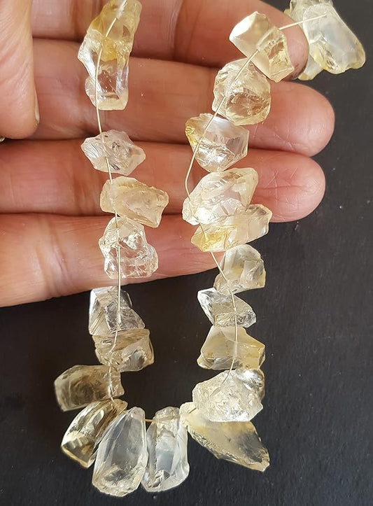 A hand holding a cluster of yellow citrine gemstone beads, showcasing their rough texture and vibrant colour.