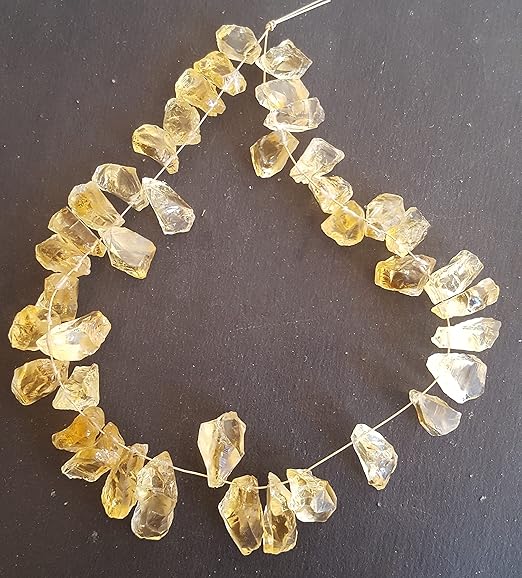 Side-drilled citrine rough bead strand featuring natural semi precious gemstone. The hand crafted crystal beads are strung in a loop on a black background.