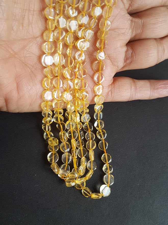 A person holding a smooth coin shaped citrine gemstone strand, showcasing its yellow smooth and elegant design.