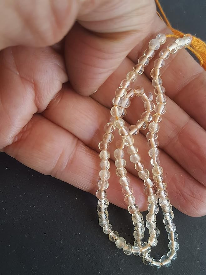 Close-up of a hand grasping a bunch of smooth Citrine natural gemstone beads, each 3.5mm in diameter.