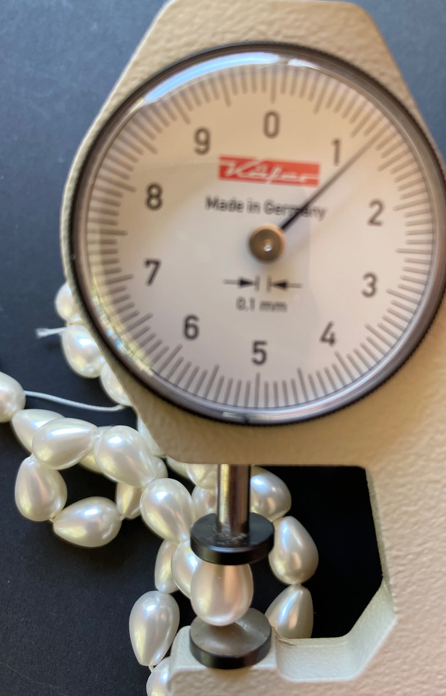 Dial Gauge rests next to a beautiful pearl bead, highlighting its measurement.