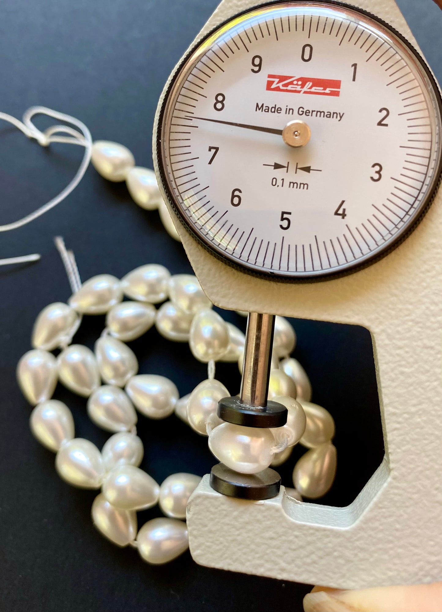 Close-up view of a dial gauge and a pearl bead featuring cone pearls, emphasising their measurement.