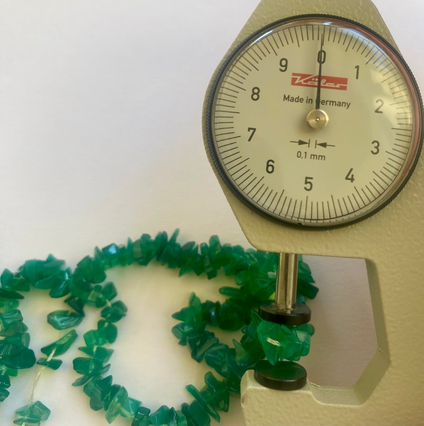 A dial gauge measures the Green Onyx Uncut Chips 5-10mm gemstone.
