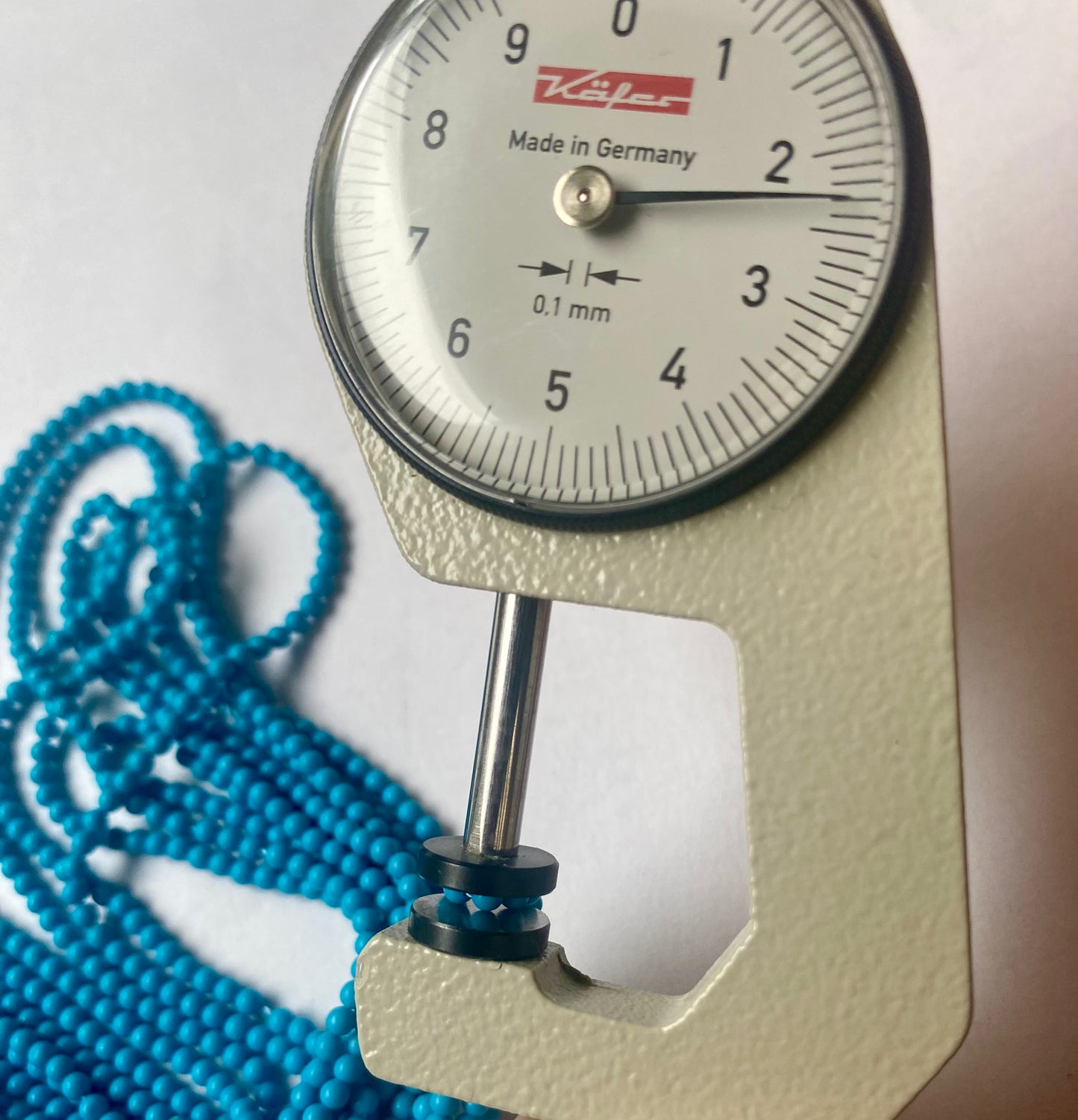 A dial gauge measures the Howlite Turquoise Smooth Round 2.3mm gemstone.